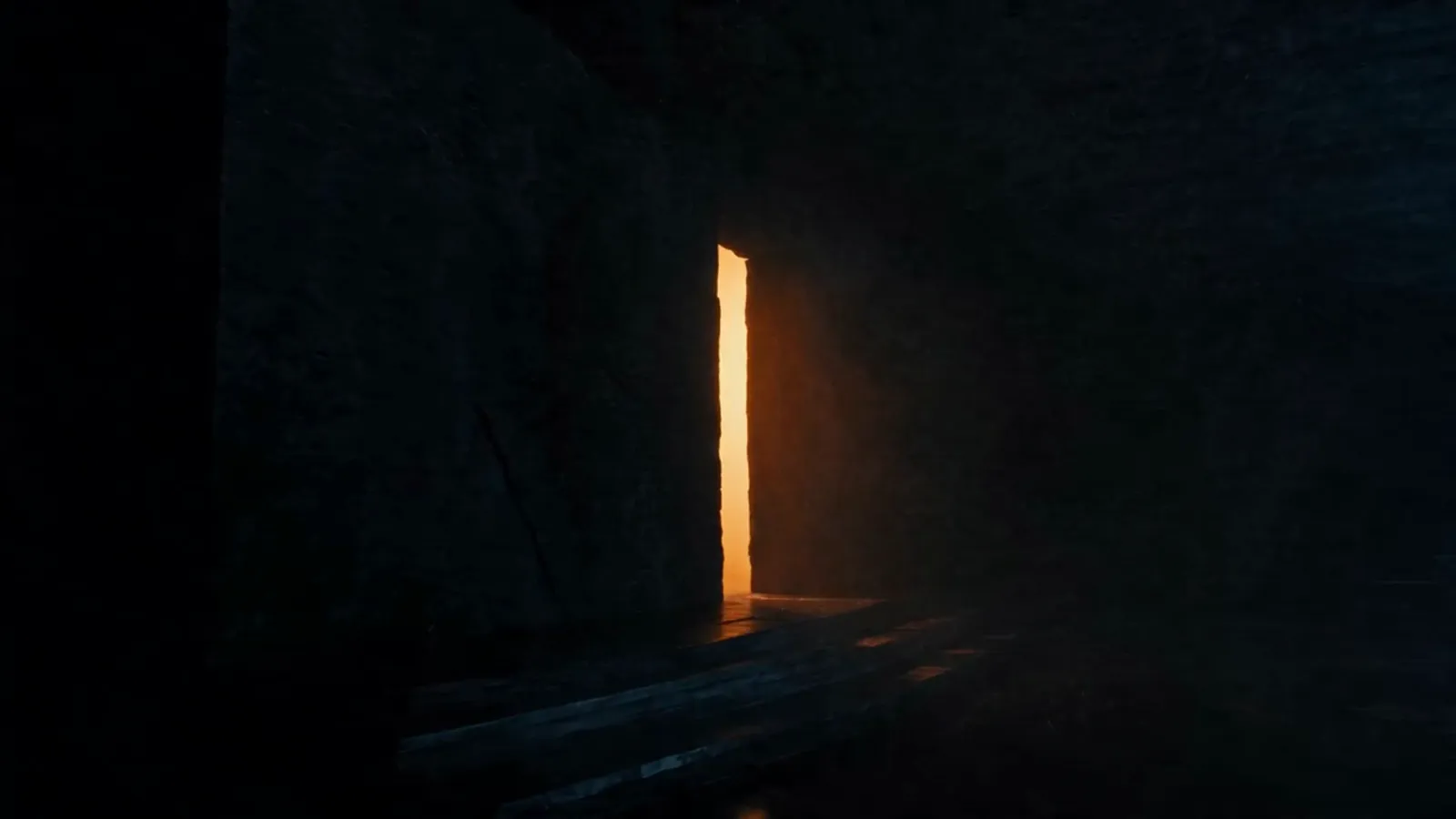 A slow push through a dark stone corridor into warm portal light